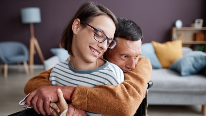 Loving father hugging smiling girl with disability at home