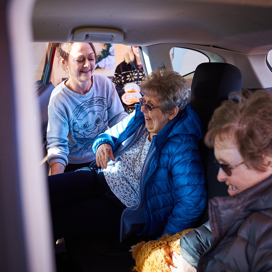 Care worker helping two elderly female participants settle into car