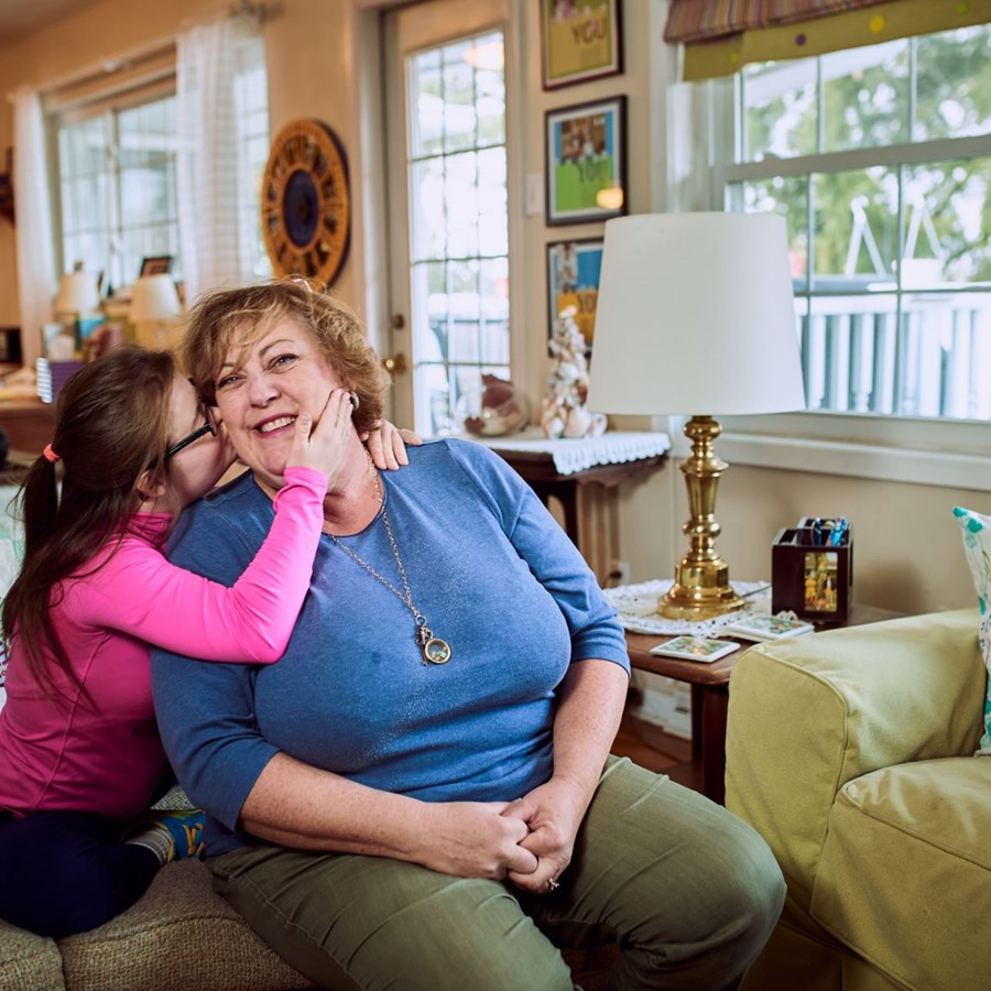 Young female participant hugging and kissing her mother while sitting on the couch 