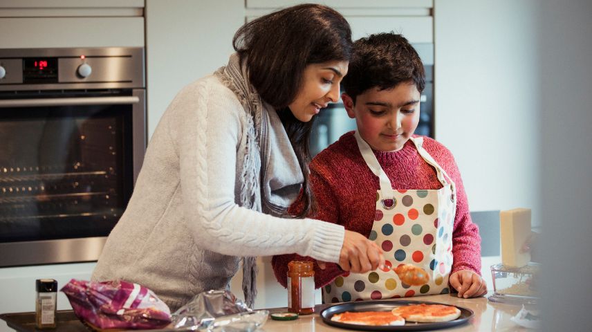 A child and mother are engaged in a cooking activity, with the child concentrating on making a pizza. The warmth and connection in the kitchen highlight the multisensory learning environment beneficial for individuals with autism.