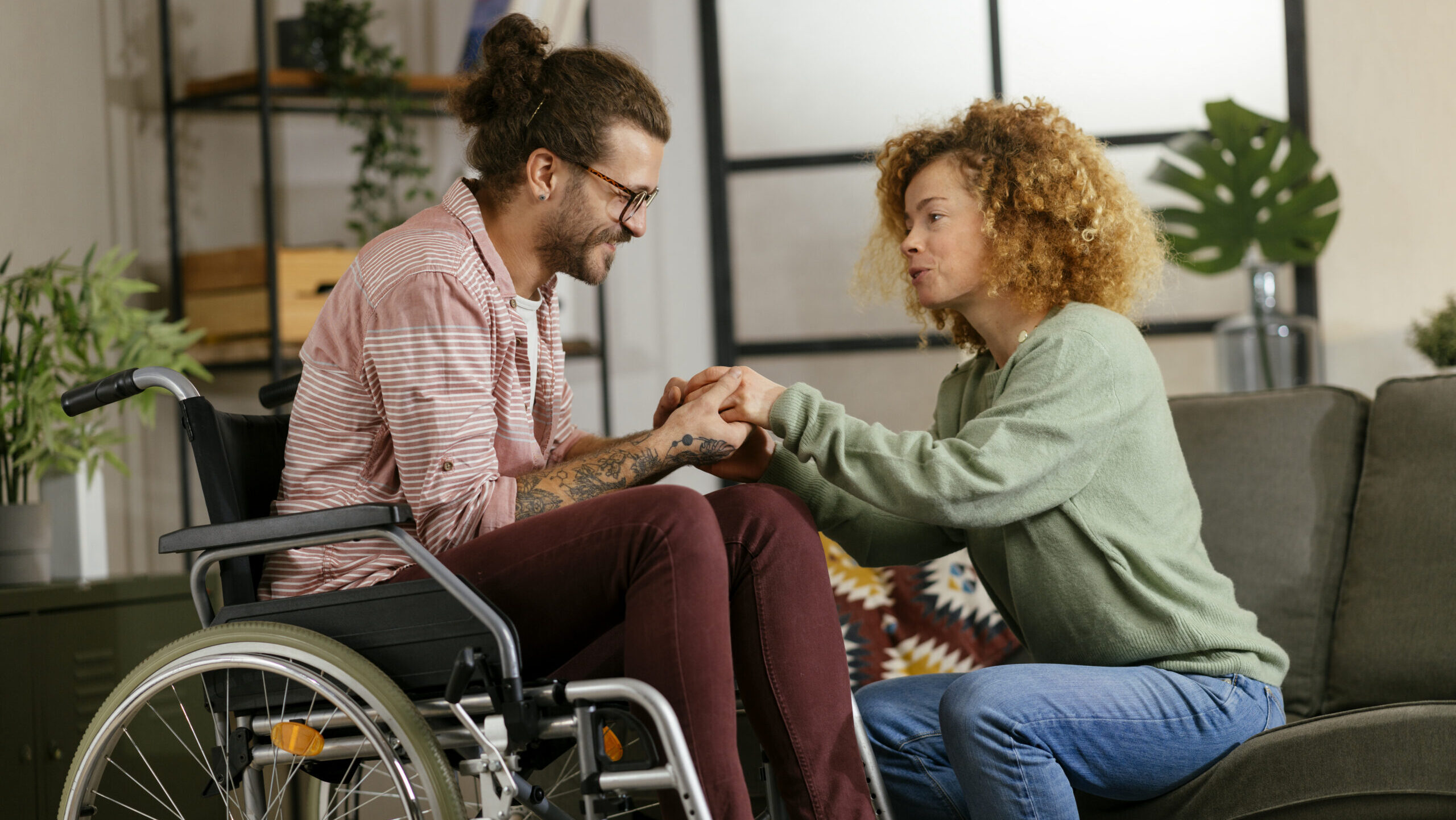 Young adult man in wheelchair holding hands with woman helping