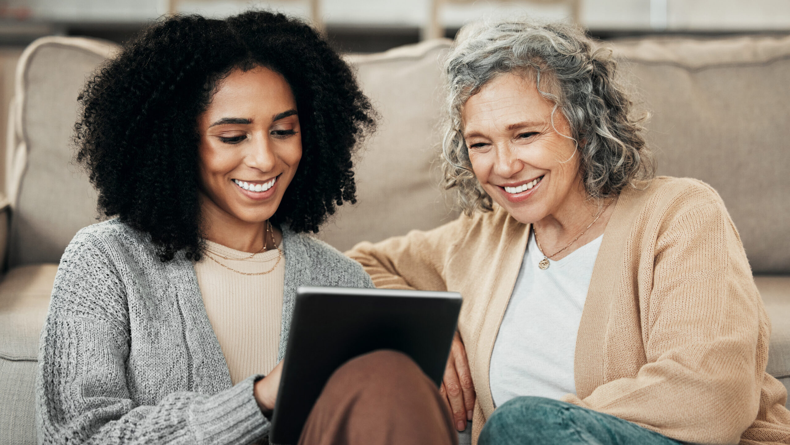 two women smiling and looking at a tablet reviewing home health care services options