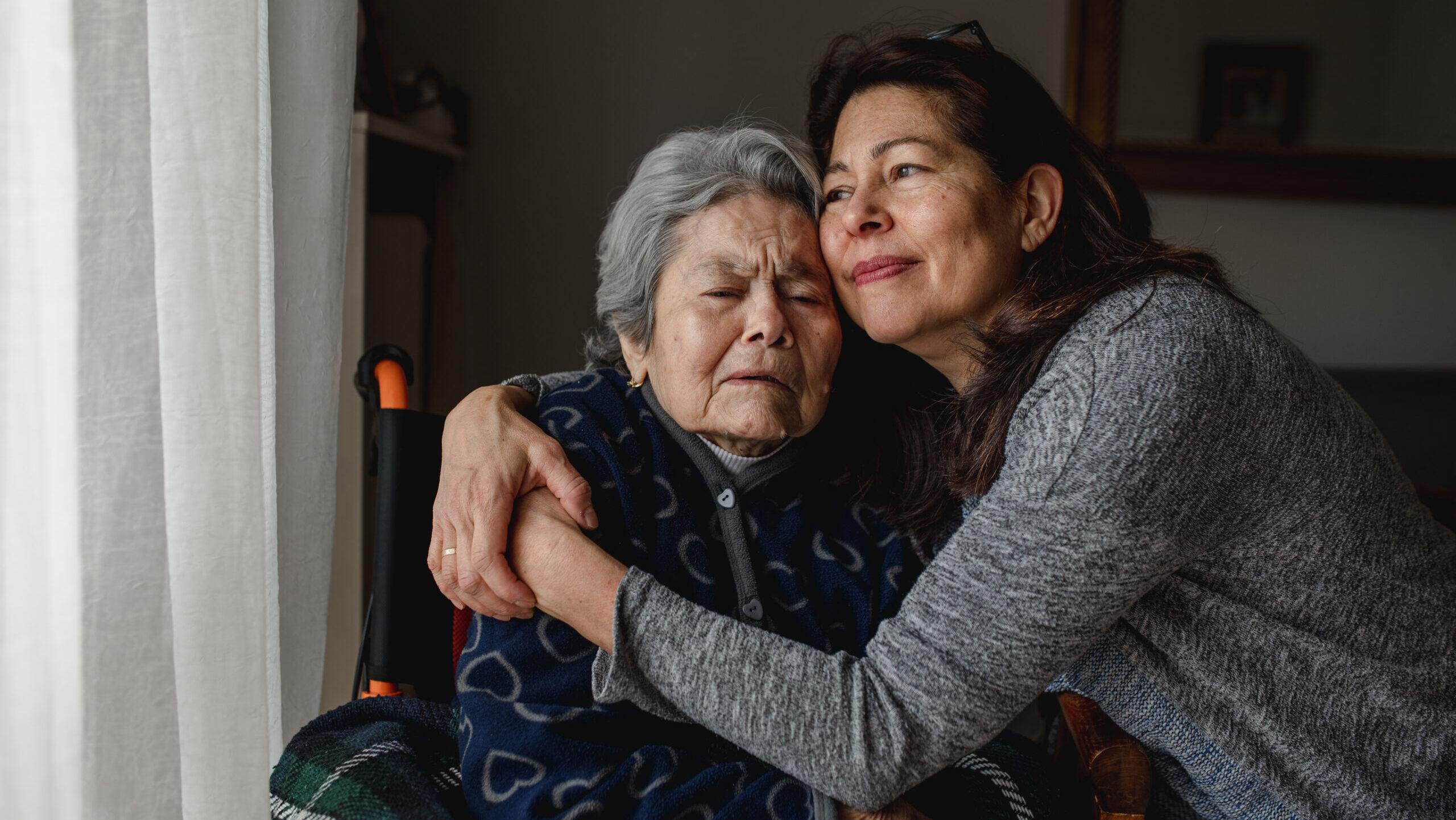 female caregiver hugging senior woman in wheelchair