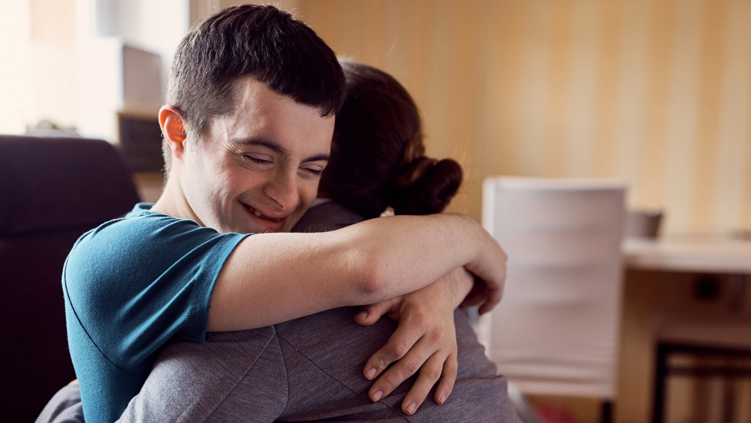 Happy man with down syndrome embracing his caregiver during home visit.