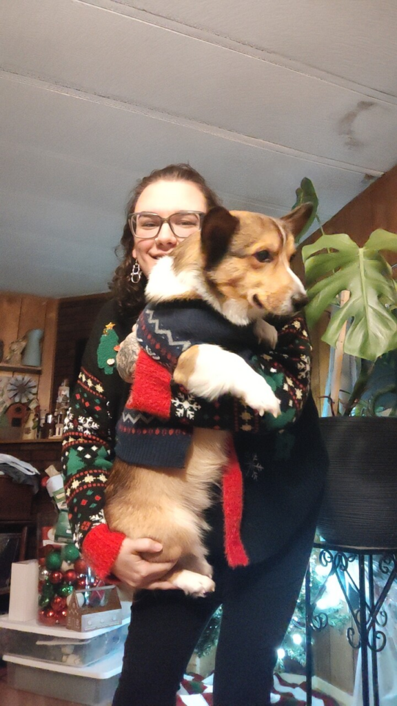 Female PPL employee holding a corgi, both dressed in Christmas sweaters