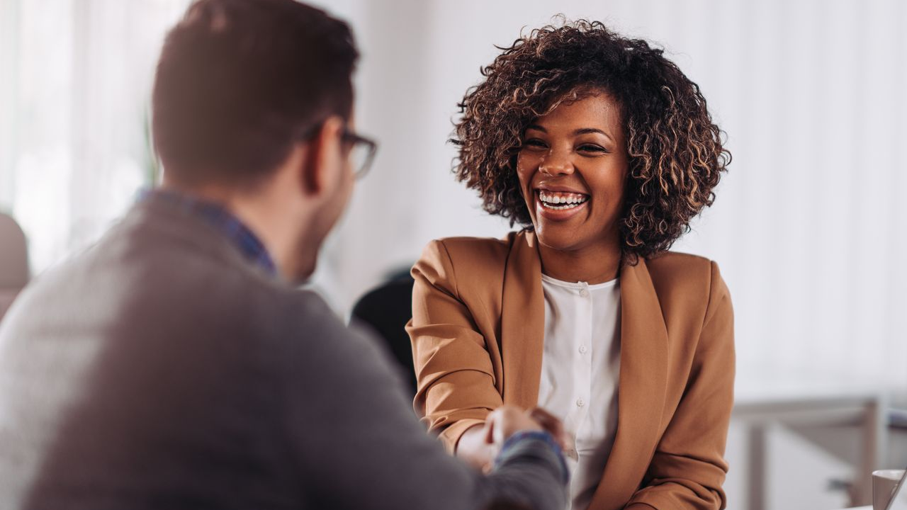 woman with short, curly, dark hair shaking the hand of a man with classes, smiling