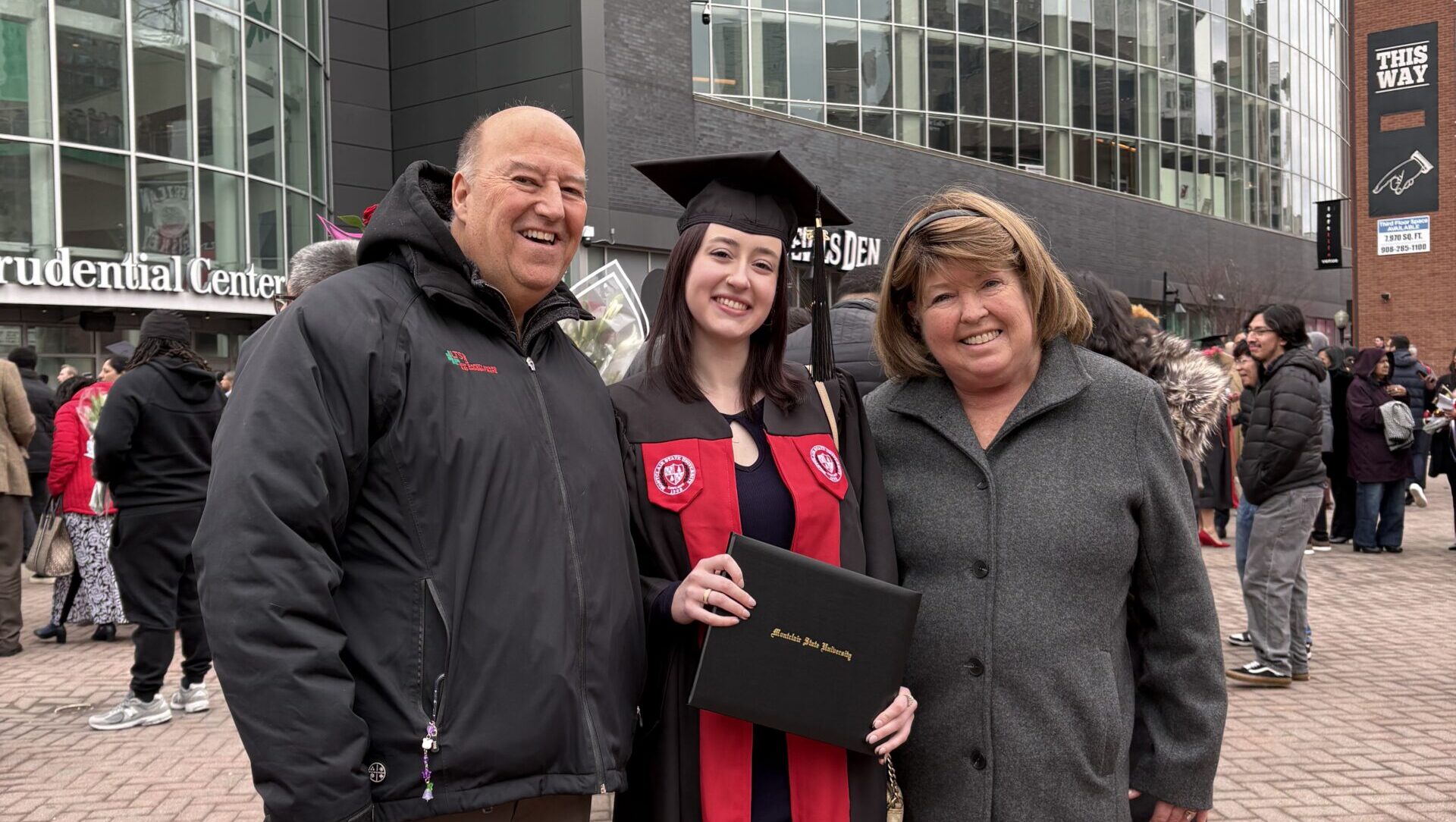 female PPL employee at her college graduation, smiling with her parents and holding her diploma