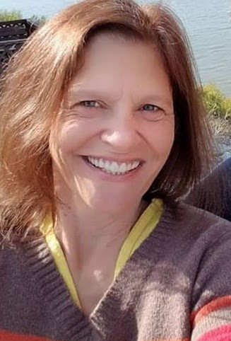 female PPL employee with brown hair, smiling in a self-taken photo, a body of water in the background