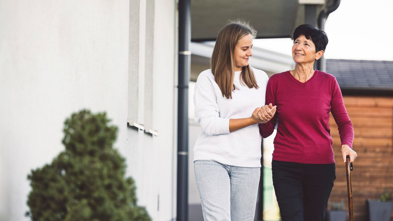 female elderly participant with short brown hair in a magenta long-sleeve shirt being helped by her female caregiver with a white shirt and medium length brown hair