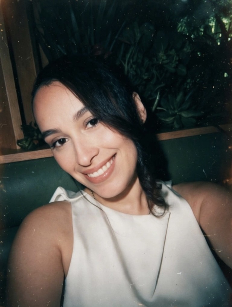 selfie of a female PPL employee with black hair, she is wearing a white shirt and smiling