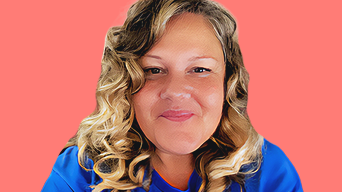 Close-up portrait of Kelly, a woman with long curly blonde hair and a warm smile, wearing a blue shirt, photographed indoors